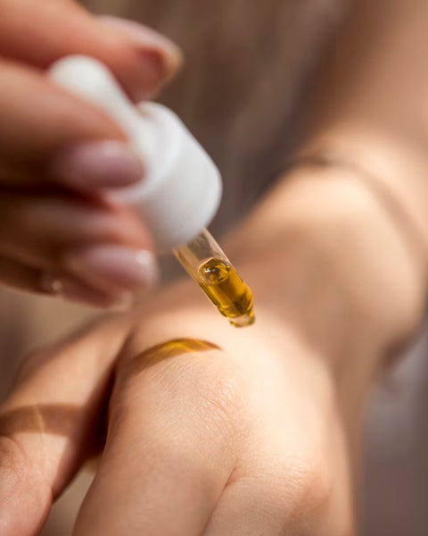 Hand applying a dropper of oil to skin